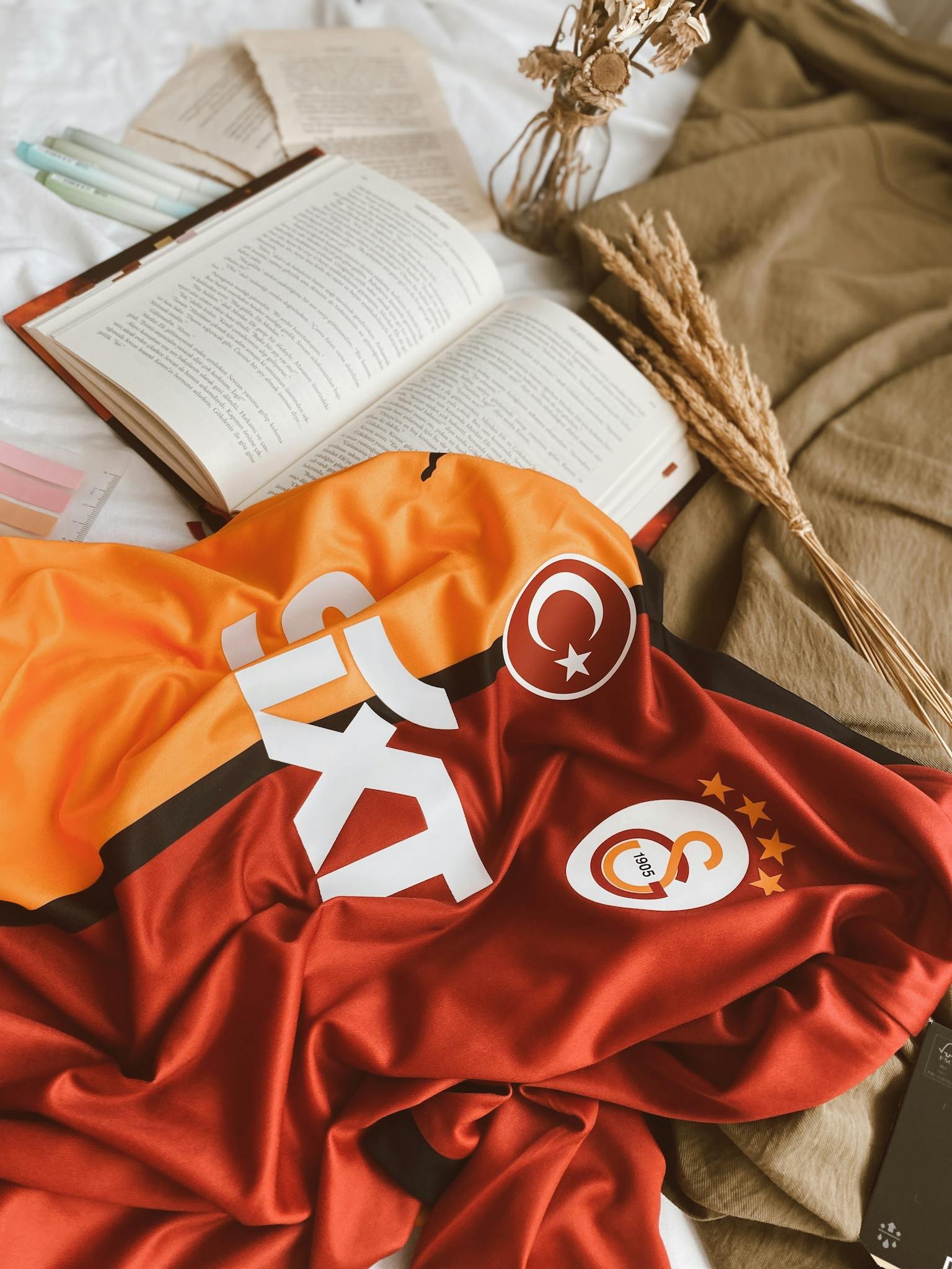 Galatasaray football jersey draped on bed near an open book, creating a cozy and relaxed atmosphere.